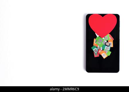 A pile of assorted used mobile SIM cards and a red paper heart on a cell phone on a white background, copy space. Cellular communication concept Stock Photo