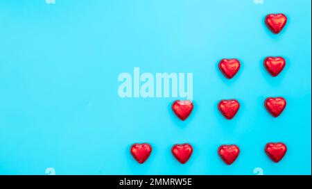 Chocolate sweets in red foil in the form of hearts on a blue background. Stock Photo