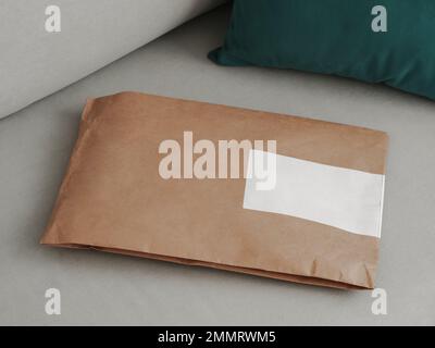 Craft paper soft pack on gray scandinavian sofa background with blank space. Shopping, Delivery, shipping, Package concept. Closed soft package on sofa in modern interior of home. Stock Photo