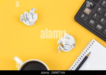Notepad, calculator, coffee cup and crumpled paper balls on a yellow background. Stock Photo