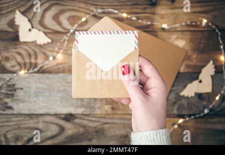 Blank postcard and envelope in female hands on a blurred wooden background. Stock Photo
