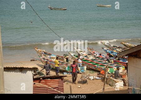 The fishing port of Bakau in the Gambia, West Africa. Fishermen and their boats and a catch of fish in a wheelbarrow. Stock Photo