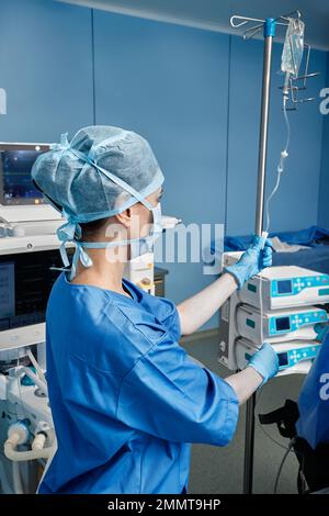 Surgery nurse wearing protective uniform preparing medical dropper for operating room patient Stock Photo