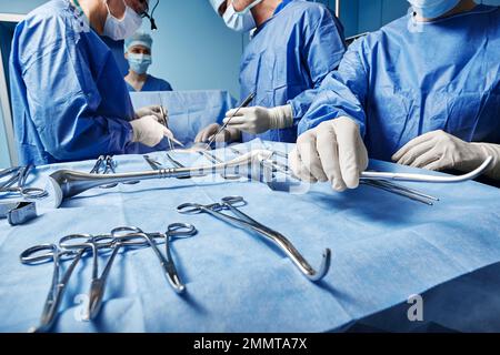 Surgical Team. Surgical nurse giving surgical scissors to male surgeon during operation in operating theatre Stock Photo