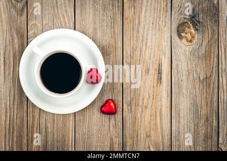 A cup of coffee and heart-shaped chocolates on a wooden background, top view. Stock Photo