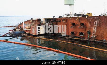 Close up of overturned oil tanker lying on its edge on the shallow water. Sunken drowned oil tanker ship after the wreck. Stock Photo