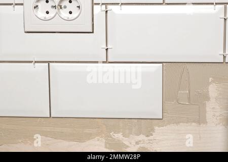 Male Worker Master Laying Ceramic Tiles on the Wall of Kitchen. Repairman Placing White Modern Tiles, Spreading Adhesive. Builder Installing Tile at R Stock Photo