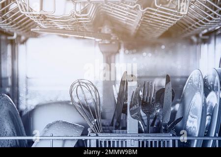 Front view of open automatic stainless steel built-in fully integrated top control dishwasher range machine with clean utensils, cutlery, glasses, dishes, plates inside in modern home kitchen Stock Photo