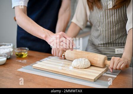 Cropped shot of a lovely couple making dough together in the kitchen, kneading raw dough with a rolling pin. Stock Photo