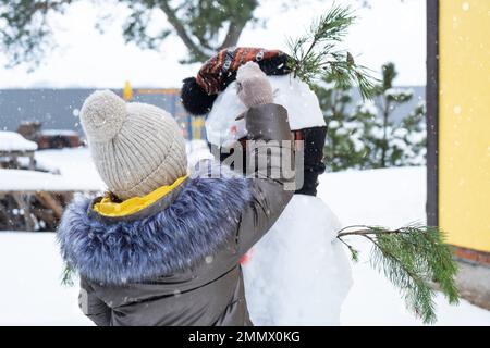 A child paints a snowman's face with paints - winter entertainment and creativity, sculpting a snowman in winter outdoor. Stock Photo