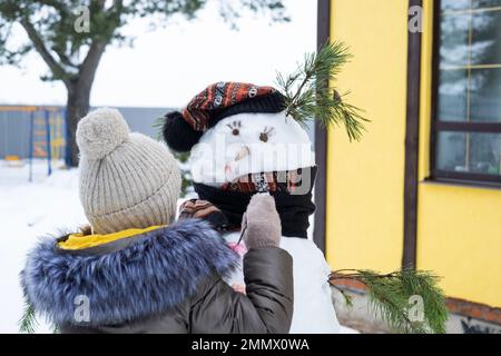 A child paints a snowman's face with paints - winter entertainment and creativity, sculpting a snowman in winter outdoor. Stock Photo