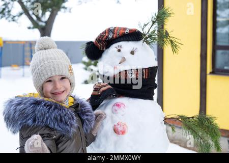 A child paints a snowman's face with paints - winter entertainment and creativity, sculpting a snowman in winter outdoor. Stock Photo