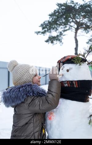 A child paints a snowman's face with paints - winter entertainment and creativity, sculpting a snowman in winter outdoor. Stock Photo