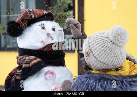 A child paints a snowman's face with paints - winter entertainment and creativity, sculpting a snowman in winter outdoor. Stock Photo