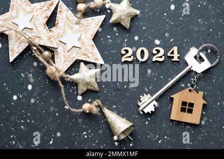House key with keychain cottage on black background with stars, snowflakes. Happy New Year 2024-wooden letters, greeting card. Purchase, construction, Stock Photo
