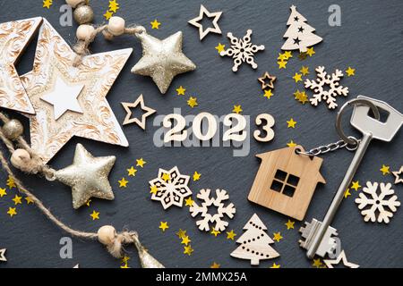House key with keychain cottage on black background with stars, snowflakes. Happy New Year 2023-wooden letters, greeting card. Purchase, construction, Stock Photo