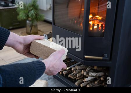 Hands kindle the hearth with economical briquettes. Fuel briquettes made of pressed sawdust for kindling the furnace - economical alternative eco-frie Stock Photo