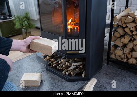 Hands kindle the hearth with economical briquettes. Fuel briquettes made of pressed sawdust for kindling the furnace - economical alternative eco-frie Stock Photo