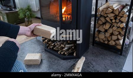 Hands kindle the hearth with economical briquettes. Fuel briquettes made of pressed sawdust for kindling the furnace - economical alternative eco-frie Stock Photo