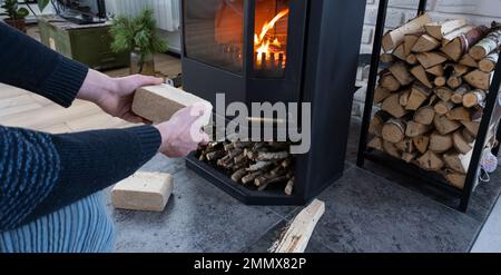 Hands kindle the hearth with economical briquettes. Fuel briquettes made of pressed sawdust for kindling the furnace - economical alternative eco-frie Stock Photo