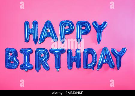 Phrase HAPPY BIRTHDAY made of blue foil balloon letters on pink background Stock Photo