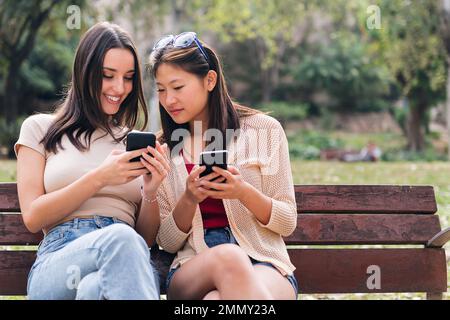 two young women smiling while looking phones Stock Photo
