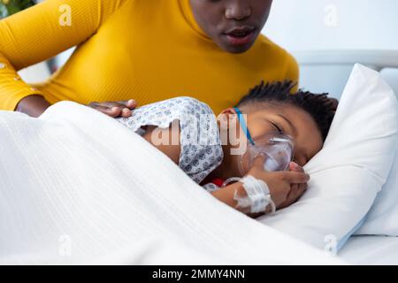 African american mother lying beside son patient on ventilator in hospital bed with copy space Stock Photo