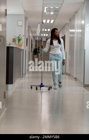 African american female patient walking through corridor with drip at hospital Stock Photo