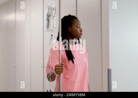 African american female patient walking through corridor with drip at hospital Stock Photo