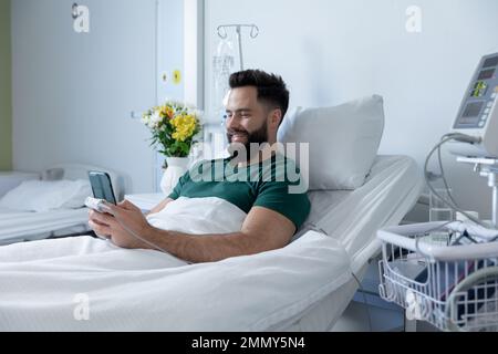 Caucasian male patient lying in bed and using smartphone at hospital Stock Photo