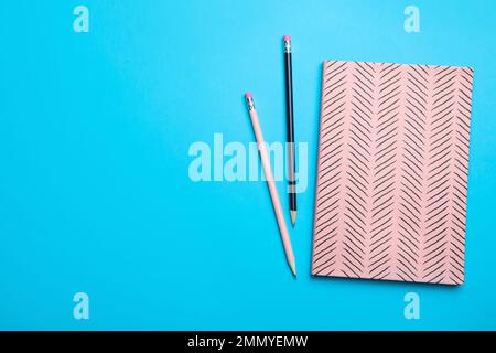 Pink notebook and pencils on light blue background, flat lay. Space for text Stock Photo