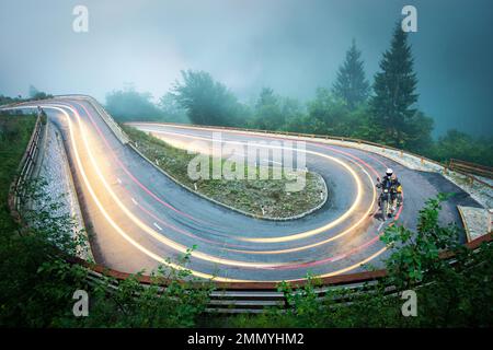 One Motorbiker on winding road with light trails. Foggy wet weather and low visibility. Dangerous Driving Conditions. Alps, Slovenia. Stock Photo