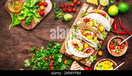 Tacos with grilled chicken, tomato salsa sauce, mango, cilantro and onion in corn tortilla on wooden board. Rustic table background, top view Stock Photo