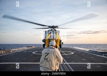 PHILIPPINE SEA (Sept. 23, 2022) – Boatswain’s Mate 2nd Class Christopher Treanor, from Mapleton, Minnesota., signals an MH-60R Sea Hawk helicopter  assigned to Helicopter Maritime Strike Squadron (HSM) 35 aboard the guided-missile destroyer USS Zumwalt (DDG 1000) while operating in the Philippine Sea, Sept. 23. Zumwalt is conducting underway operations in support of a free and open Indo-Pacific. Stock Photo