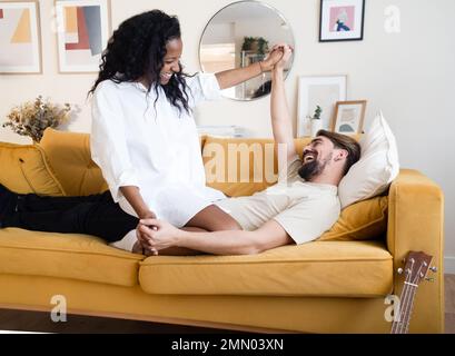 Young diverse heterosexual couple having fun on the sofa in an apartment. Stock Photo