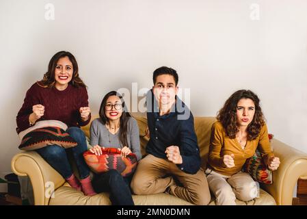 Group of scared friends gathering on sofa and watching horror movie during weekend at home Stock Photo