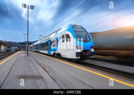 Blue high speed train in motion on the railway station at sunset Stock Photo