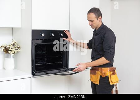 Don't delay with repair. Close-up of repairman examining oven with screwdriver in kitchen with tool case Stock Photo