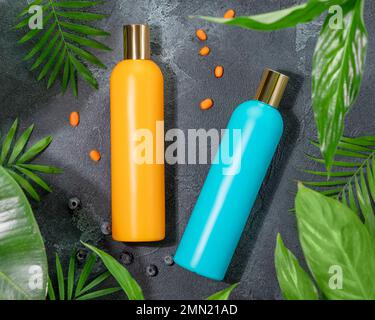 Top view photo of contrast orange and blue cosmetic bottles without label in the middle green leaves. Organic beauty product. Beauty care containers. Stock Photo