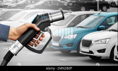 Hand with Hydrogen nozzle on a background of cars. Clean transportation concept Stock Photo