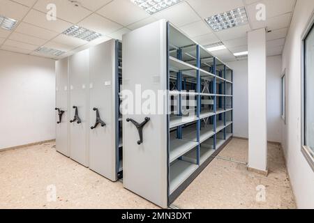 Abandoned warehouse with old shelving on rusty skids for storage. The floor is littered with rubbish not removed from the previous owners. On the Stock Photo