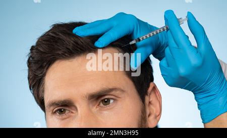 Handsome man receiving injections in his head, having mesotherapy session, blue background, panorama Stock Photo
