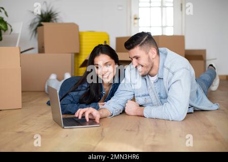 Smiling Young Couple Using Laptop After Moving To Their New Home Stock Photo