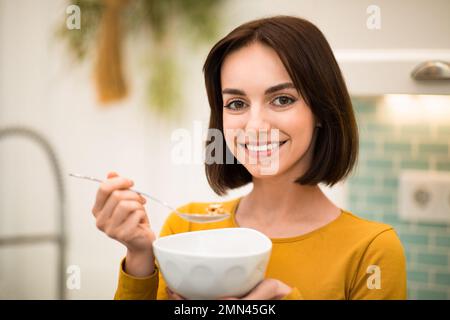 Closeup of cheerful young woman enjoying breakfast cereals at home Stock Photo