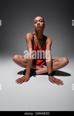 full length of brunette african american sportswoman sitting with crossed legs on grey Stock Photo