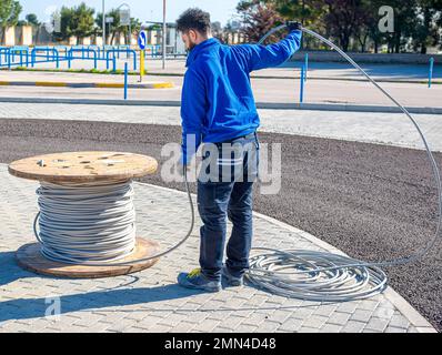 Worker inserts a yellow and green electric cable on the ground in an inspection line of the power line Stock Photo