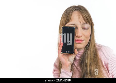 Portrait of a woman with closed eyes holding a smartphone in front of half face isolated on a white background. High quality photo Stock Photo