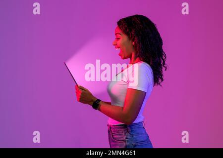 Surprised Black Woman Looking At Digital Tablet With Glowing Screen Stock Photo