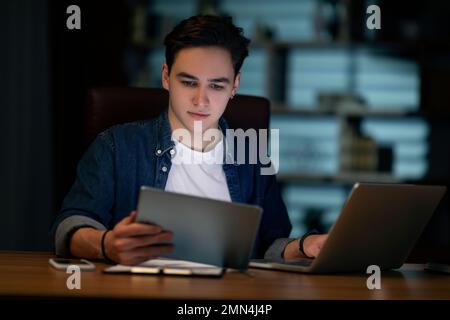 Concentrated young man employee working at office in evening Stock Photo