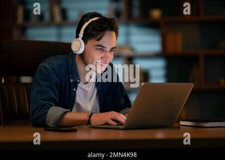 Young smiling man working on laptop late at night Stock Photo